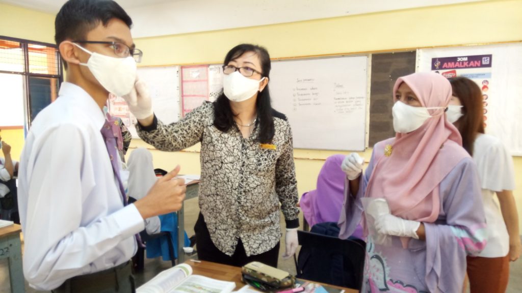 Elaine Yue adjusting the face mask of a school goers.